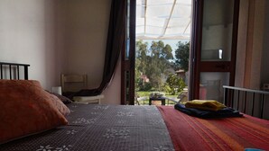 A bedroom with a bed, a chair, a small table, and a view of the outdoors through a large window. - "Pride and Prejudice" - Residences Gattopardu (castiadas)