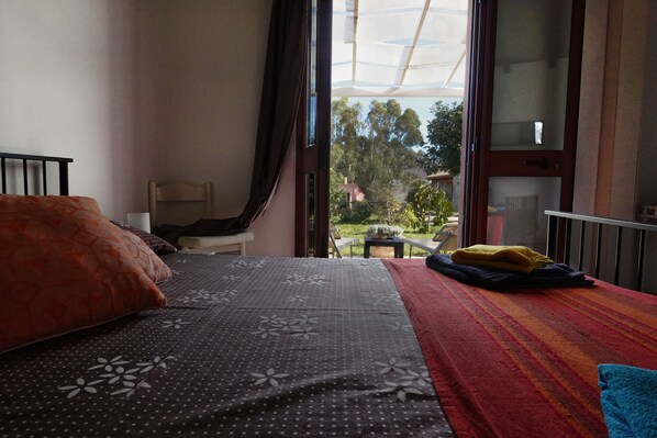 A bedroom with a bed, a chair, a small table, and a view of the outdoors through a large window.