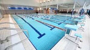 A large indoor swimming pool with multiple lanes, starting blocks, and spectator seating. - Ebor Cosy Homli Parking Wifi Smart (Belfast)