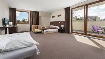 Habitación de hotel con cama, escritorio con computadora, silla, mesita y balcón con vista a edificios.