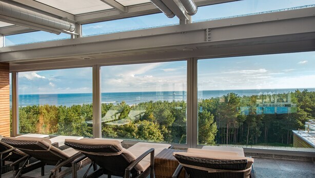 A sunlit balcony with wicker furniture and a view of the ocean.
