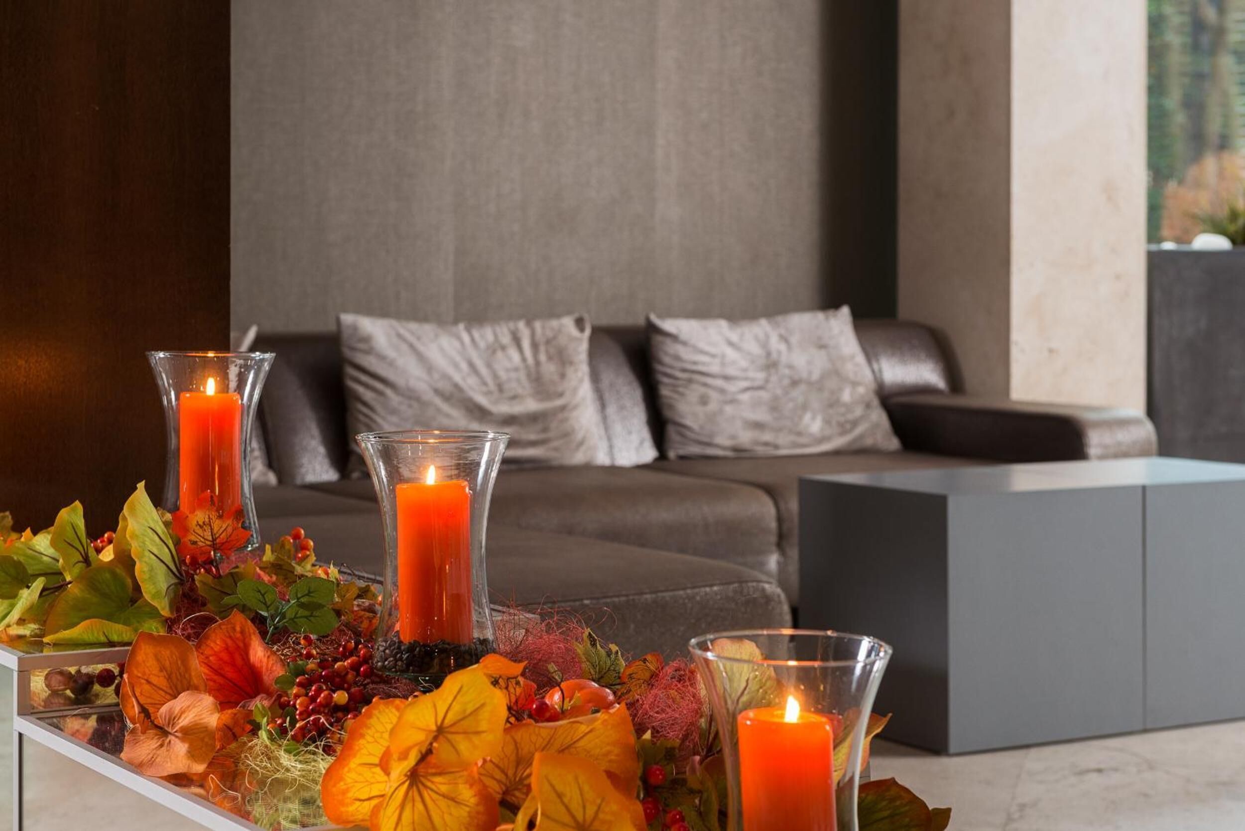 Un salon moderne avec un canapé, une table en verre décorée de bougies et des feuilles d’automne.