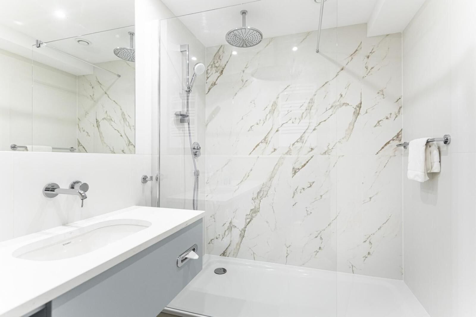 Un baño moderno con pared de mármol, cabina de ducha de vidrio y lavamanos blanco.