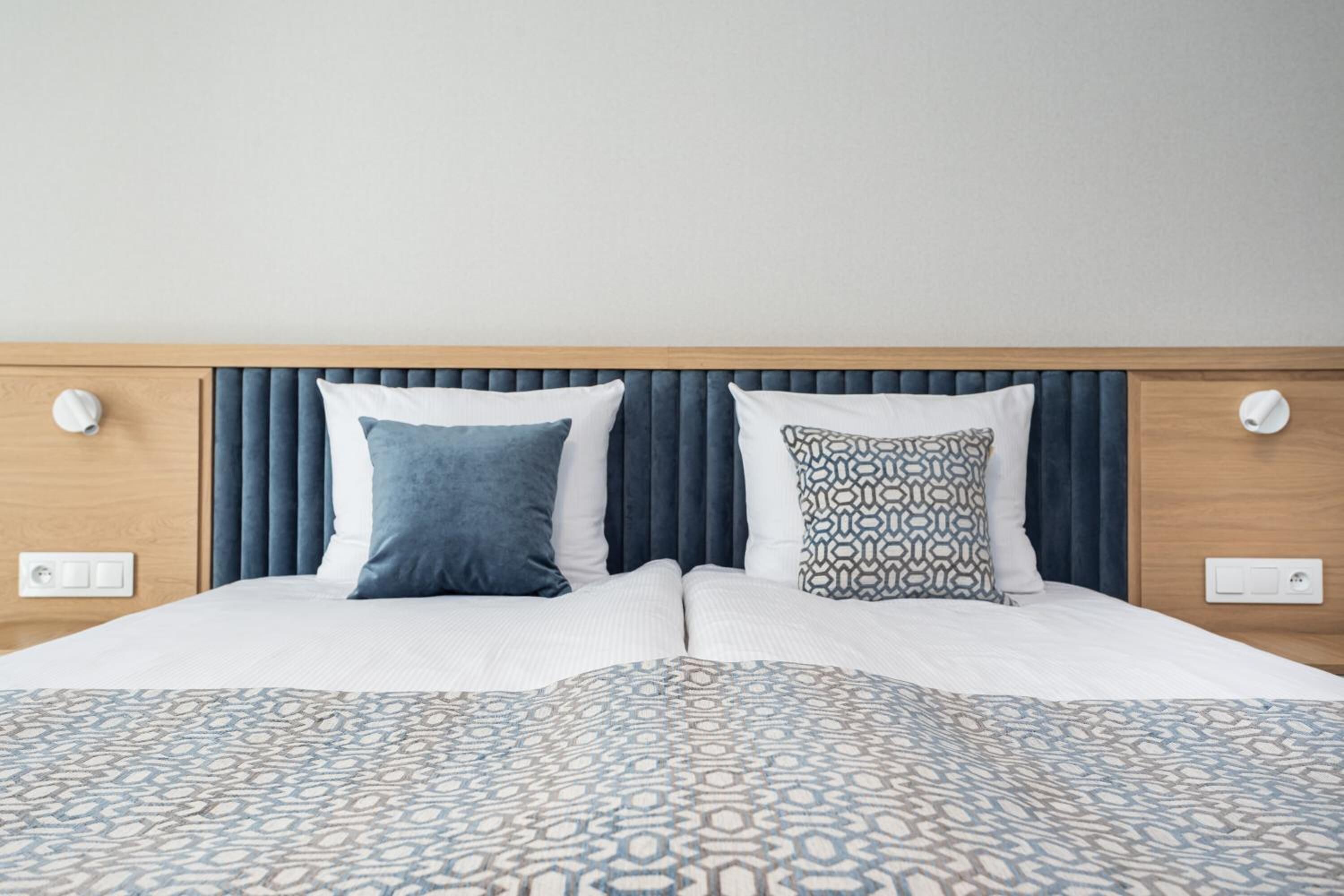 A neatly made double bed with a patterned bedspread, a headboard with vertical slats, and two bedside lamps.