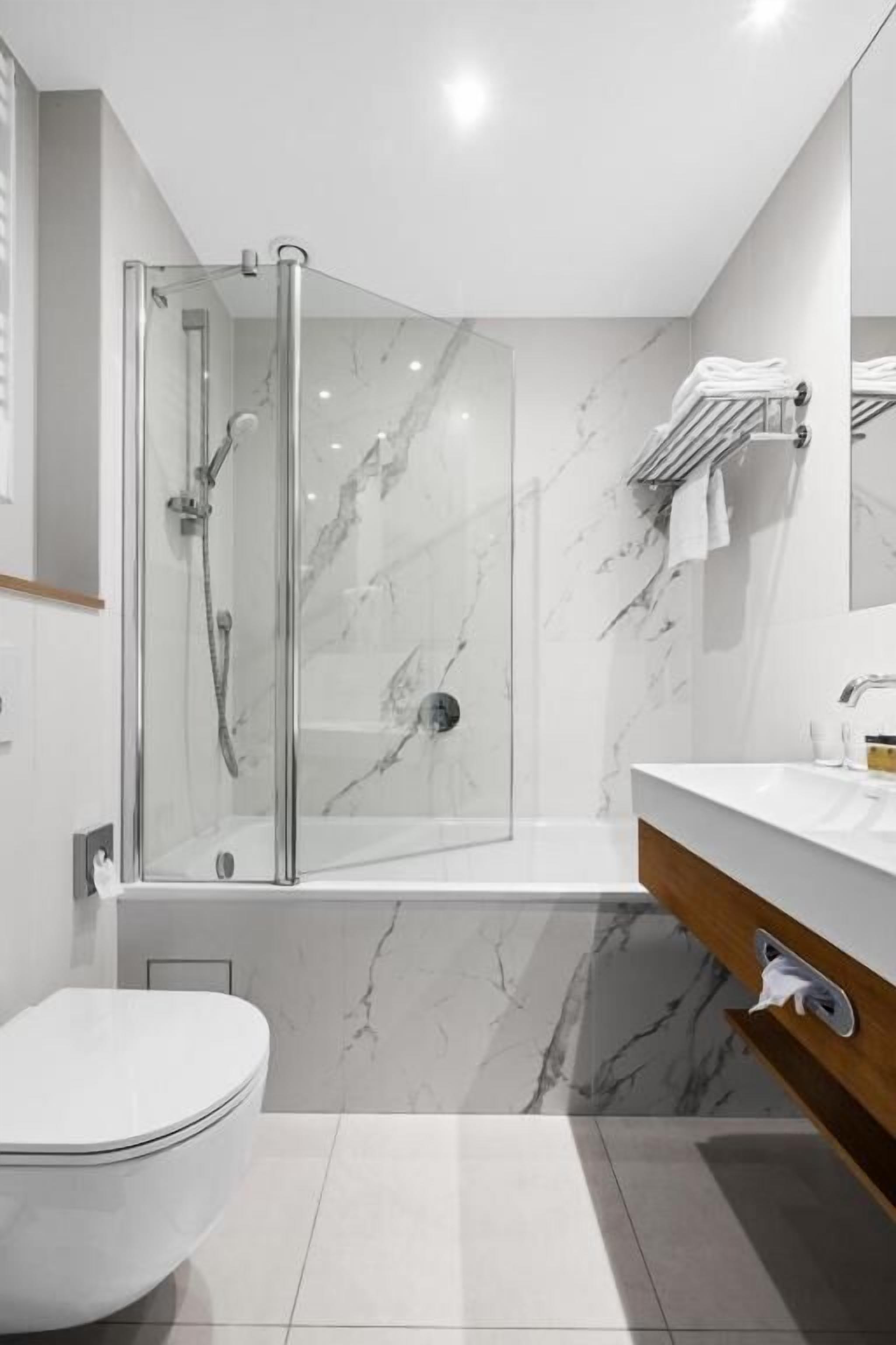 Un baño moderno con ducha de vidrio, inodoro blanco y piso de mármol.