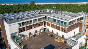 A modern building with a rooftop terrace, large windows, and a view of the beach.