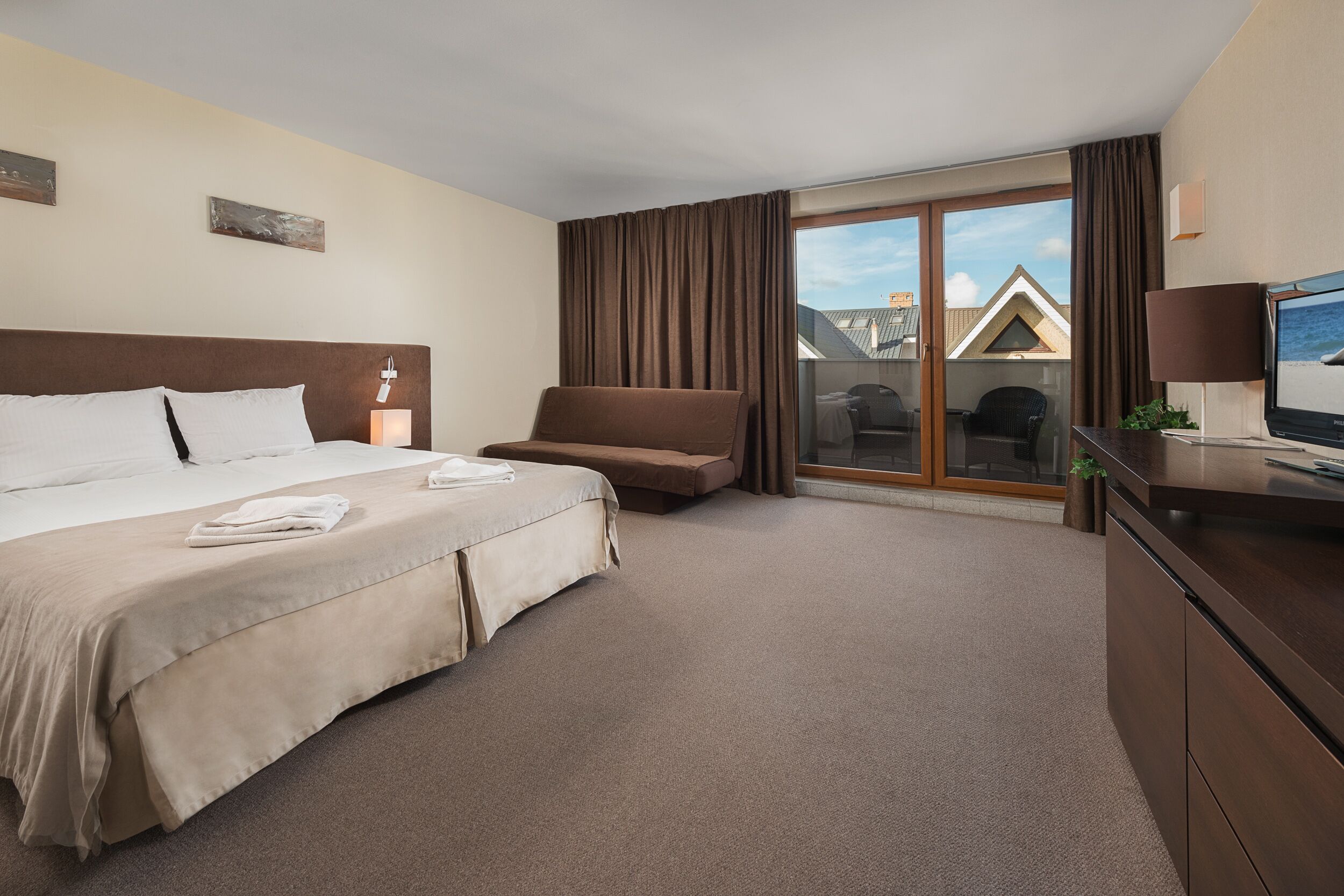 Habitación de hotel con una cama grande, un sofá, un escritorio con televisor y vistas al exterior.