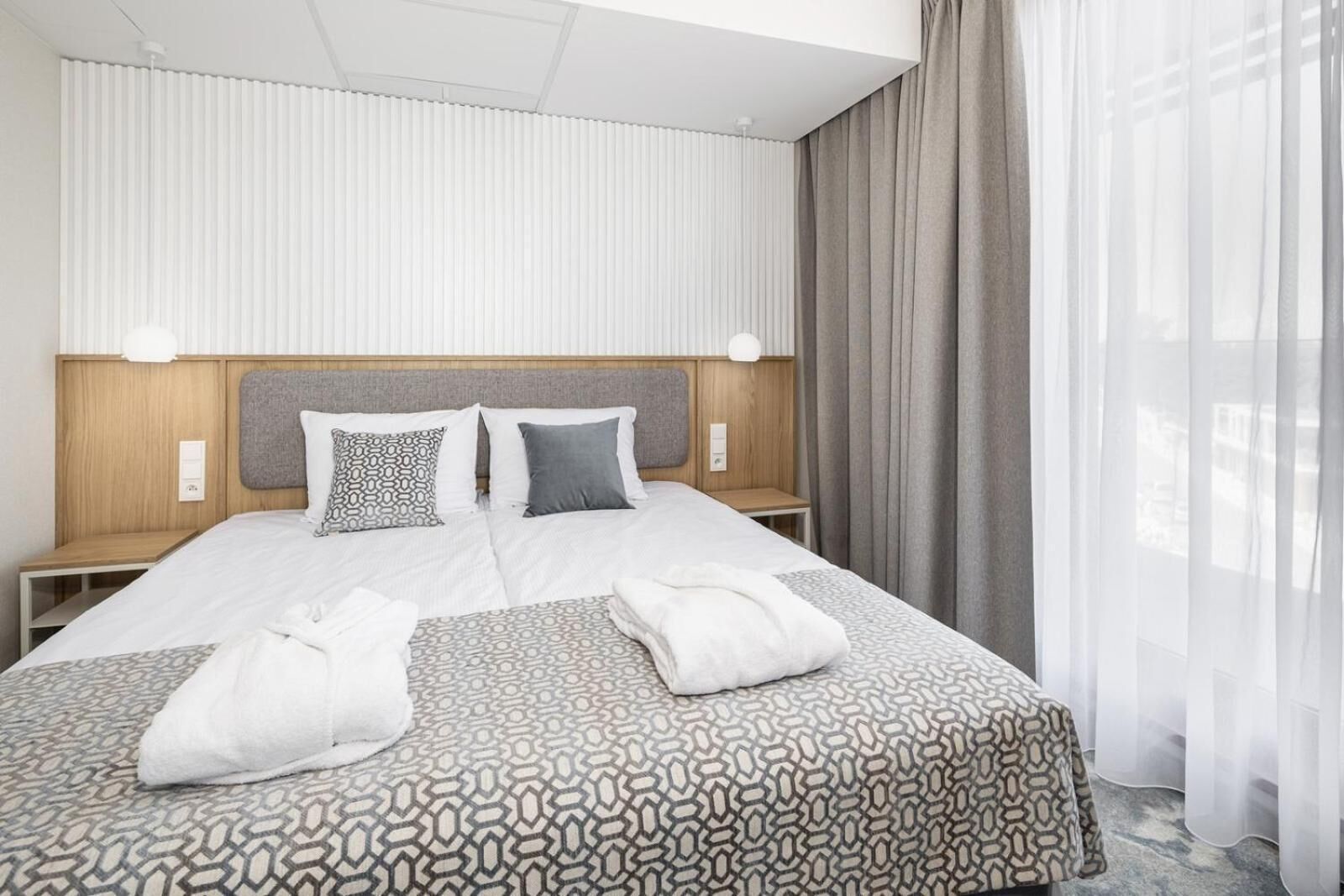 Una camera d'albergo con un letto grande, due comodini, una testiera e una finestra con tende.