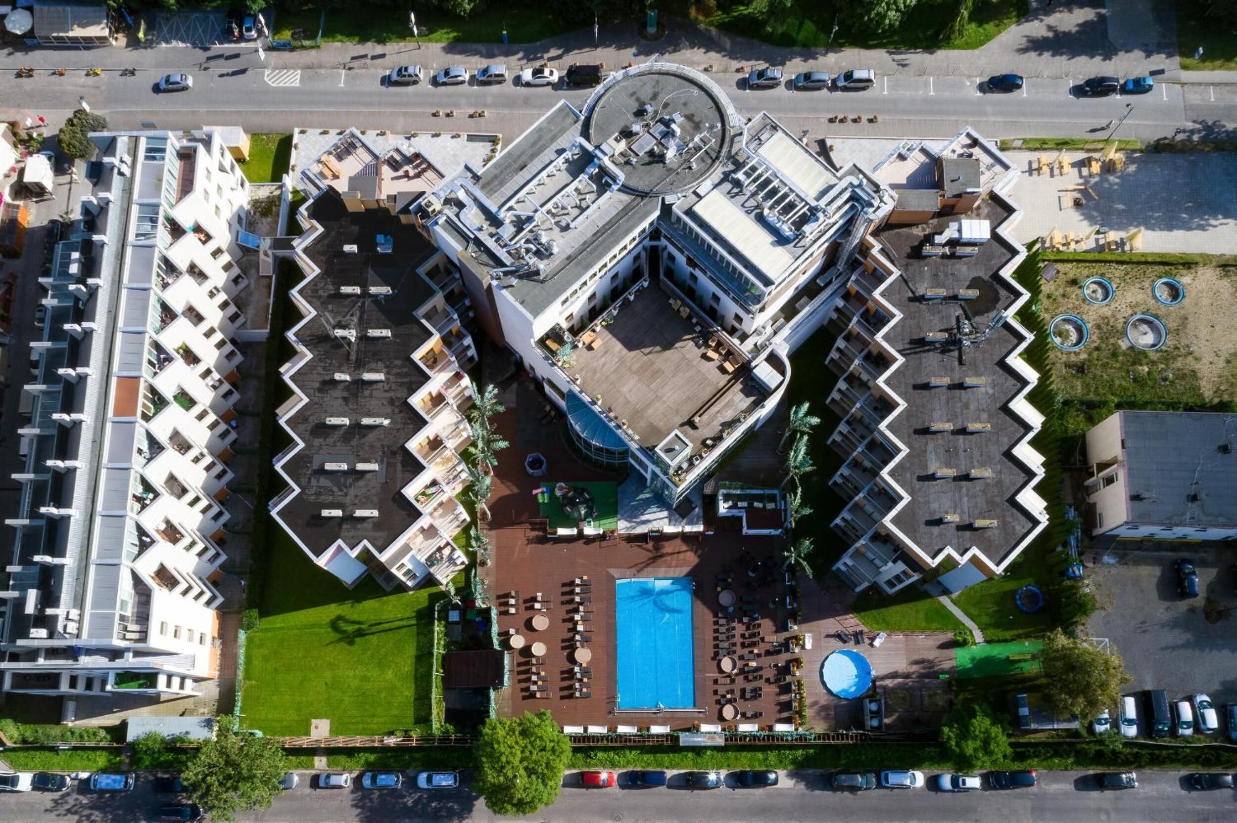 An aerial view of a hotel with a central courtyard, multiple balconies, and a swimming pool.