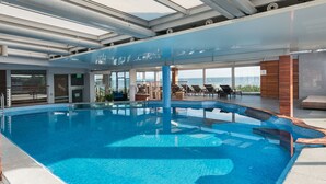 A large indoor swimming pool with clear blue water, surrounded by lounge chairs and a view of the sea.