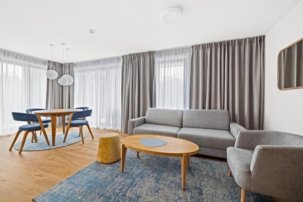 A modern living room with a grey sofa, a round coffee table, and a dining area with a wooden table and blue chairs.
