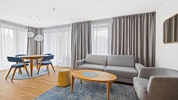 A modern living room with a grey sofa, a round coffee table, and a dining area with a wooden table and blue chairs.