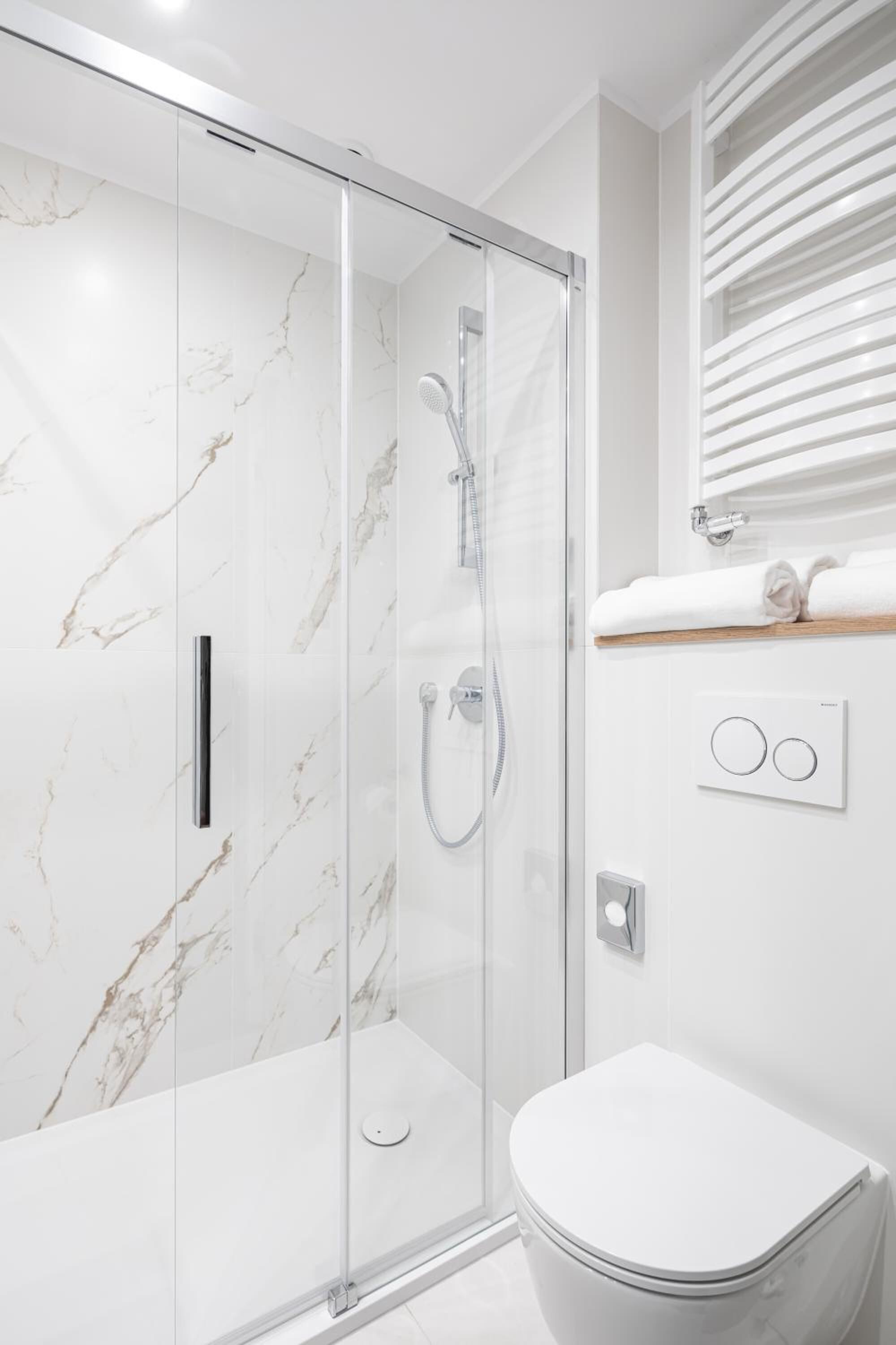 Une salle de bain moderne avec une douche à parois de verre, des toilettes blanches et un porte-serviettes intégré.