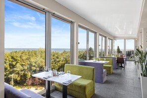 Un restaurant moderne doté de grandes fenêtres offrant une vue sur la mer et les arbres.