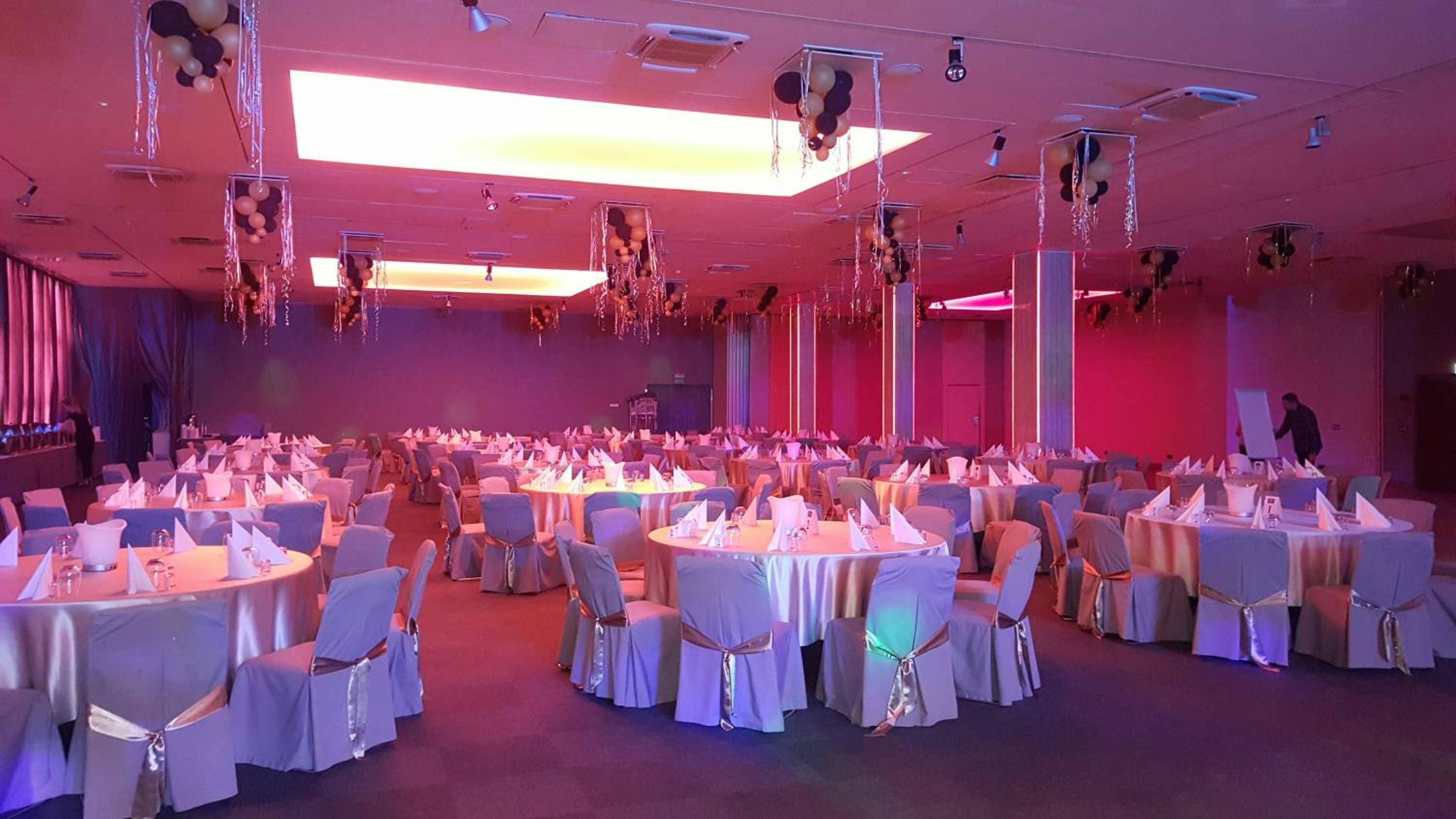 Un salón de banquetes con mesas redondas preparadas para un evento formal, con manteles blancos y sillas con lazos.