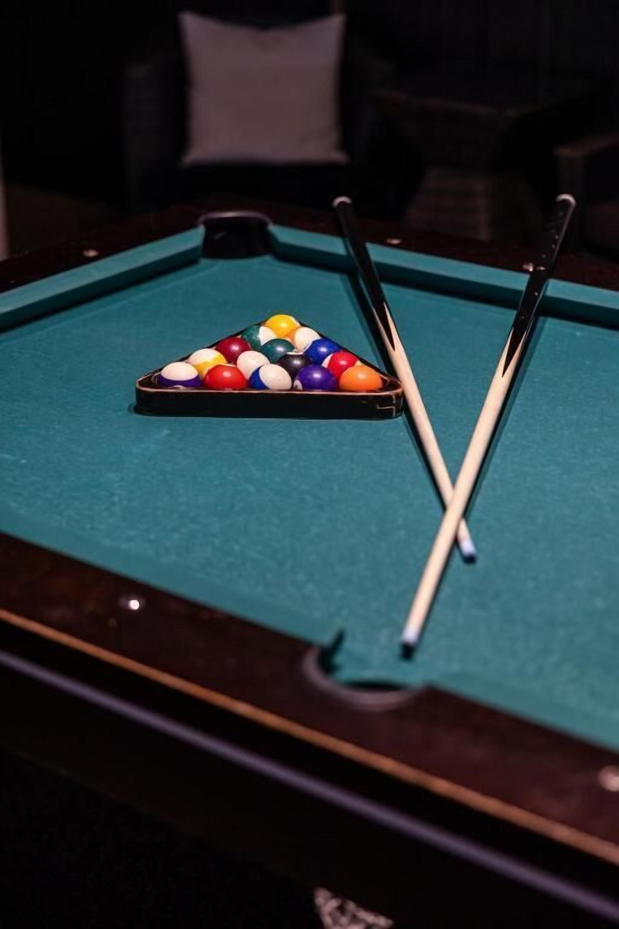 A pool table with a triangular rack of billiard balls and two pool cues.