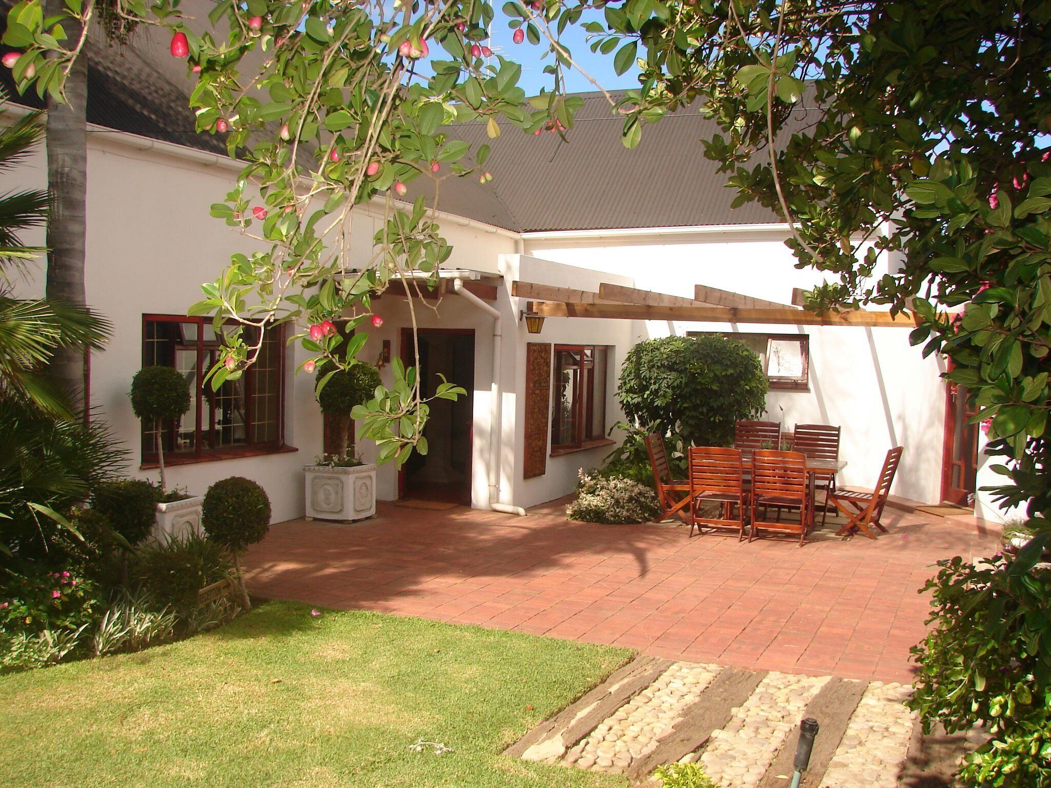 A covered patio with a wooden table and chairs, surrounded by potted plants and a small garden.