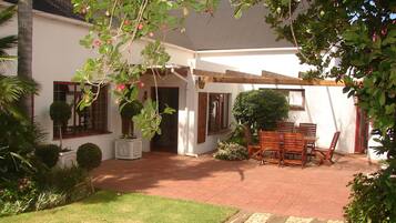 A covered patio with a wooden table and chairs, surrounded by potted plants and a small garden.