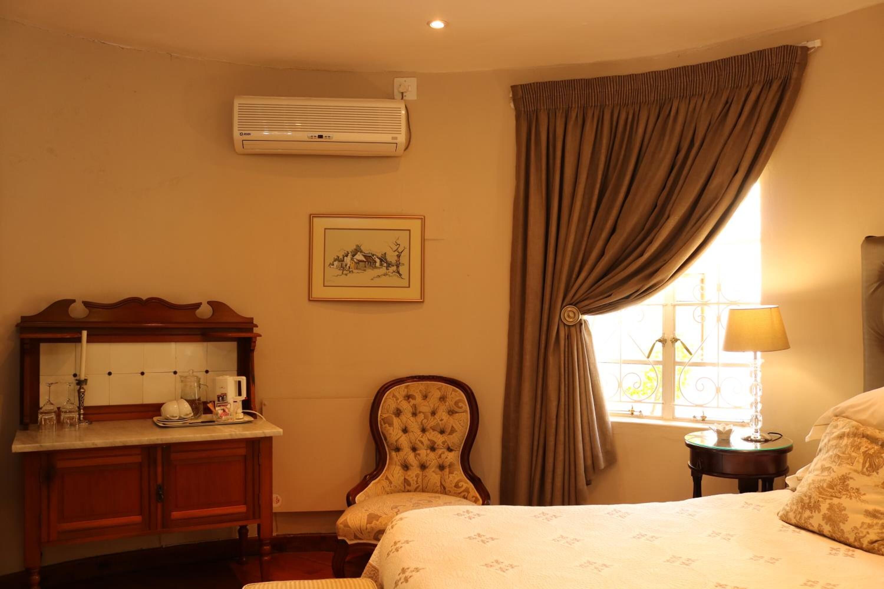 Habitación de hotel con cama, una silla, escritorio con espejo, un cuadro en la pared y ventana con cortinas.