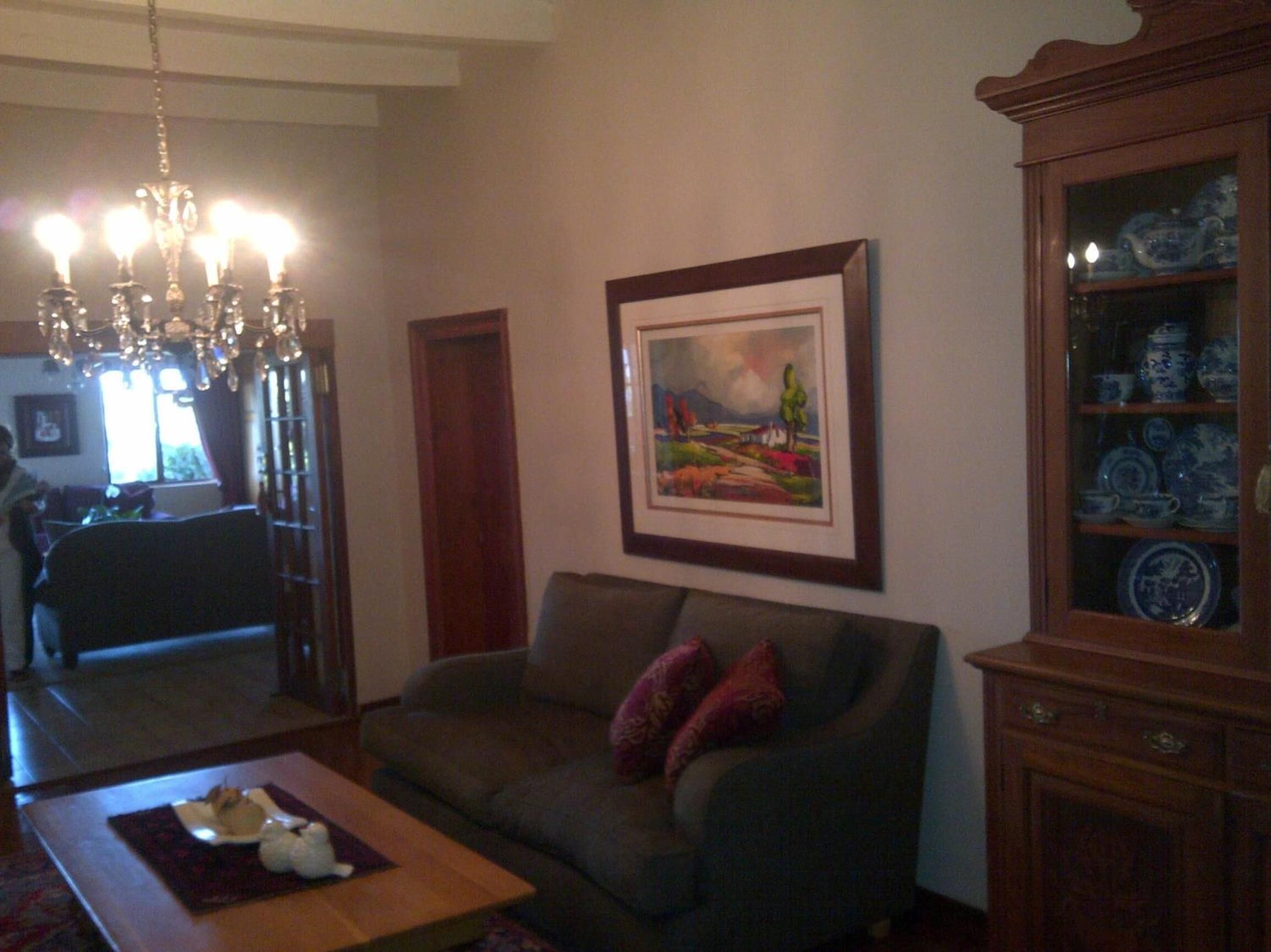 A living room with a sofa, a coffee table, a chandelier, a framed painting, and a cabinet with blue and white dishes.