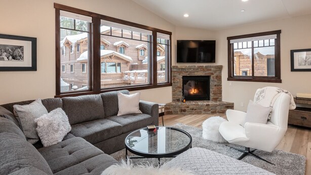 A modern living room with a gray sectional sofa, a white armchair, a glass coffee table, and a stone fireplace.