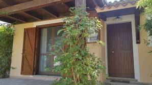 Un bâtiment avec une porte en bois, une fenêtre et un petit arbre devant.