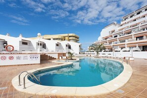 A swimming pool surrounded by white buildings with balconies, a lifebuoy, and safety signs. - Home2Book Paradise Costa Adeje, Pool (Playa de las Americas)