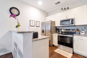 A modern kitchen with white cabinets, stainless steel appliances, a clock, and decorative items.