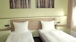 A hotel room with two single beds, a wooden headboard, bedside tables with lamps, and artwork on the wall.