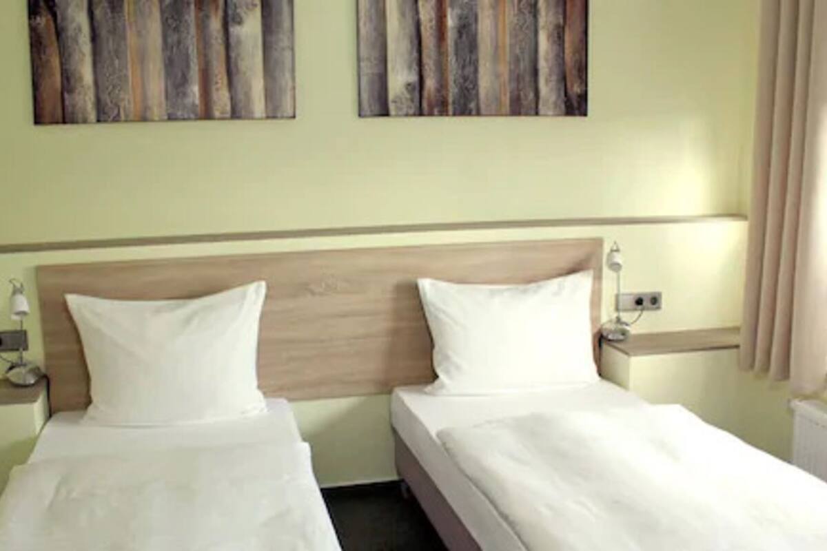 A hotel room with two single beds, a wooden headboard, bedside tables with lamps, and artwork on the wall.