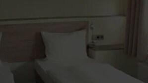 A standard hotel room with a single bed, a wooden headboard, and a nightstand with a lamp.