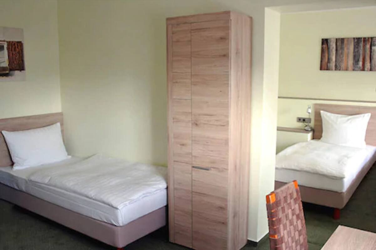 A hotel room with a single bed, a wooden wardrobe, and a small table.