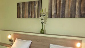 A double bed with white linens, two bedside tables with lamps, and a vase with flowers on the wall.