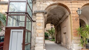 A stone building with a glass elevator, a covered walkway, and potted plants. - Ajutamicristo by DomuSicily (Palermo)