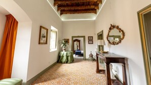 A hallway with a patterned floor, a wooden ceiling, a green table with a plant, a mirror, and a bed in the background. - Ajutamicristo by DomuSicily (Palermo)
