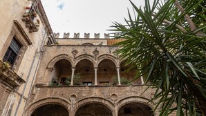 A historic building with a courtyard featuring arched walkways and a balcony with potted plants. - Ajutamicristo by DomuSicily (Palermo)