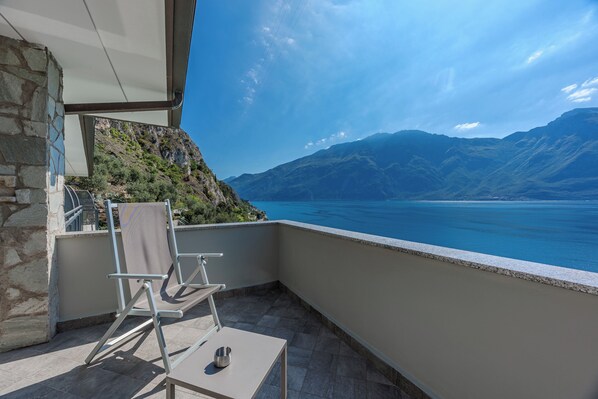 A balcony with a chair, a table, and a view of a mountainous landscape and water.