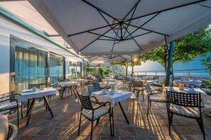 An outdoor dining area with tables and chairs, a covered section, and a view of the sea. - Relax Hotel La Gardenia & Villa Oleandra (Limone sul Garda)