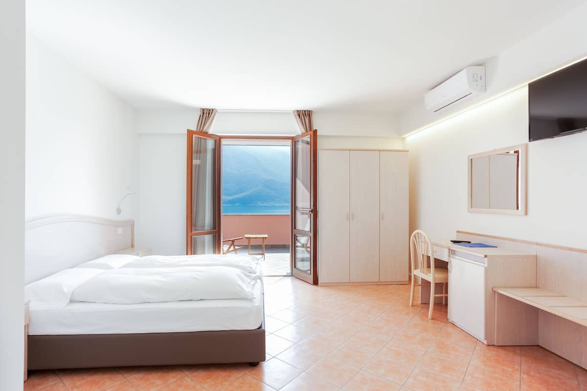 Habitación de hotel con cama, escritorio, silla, armario y vistas al exterior.