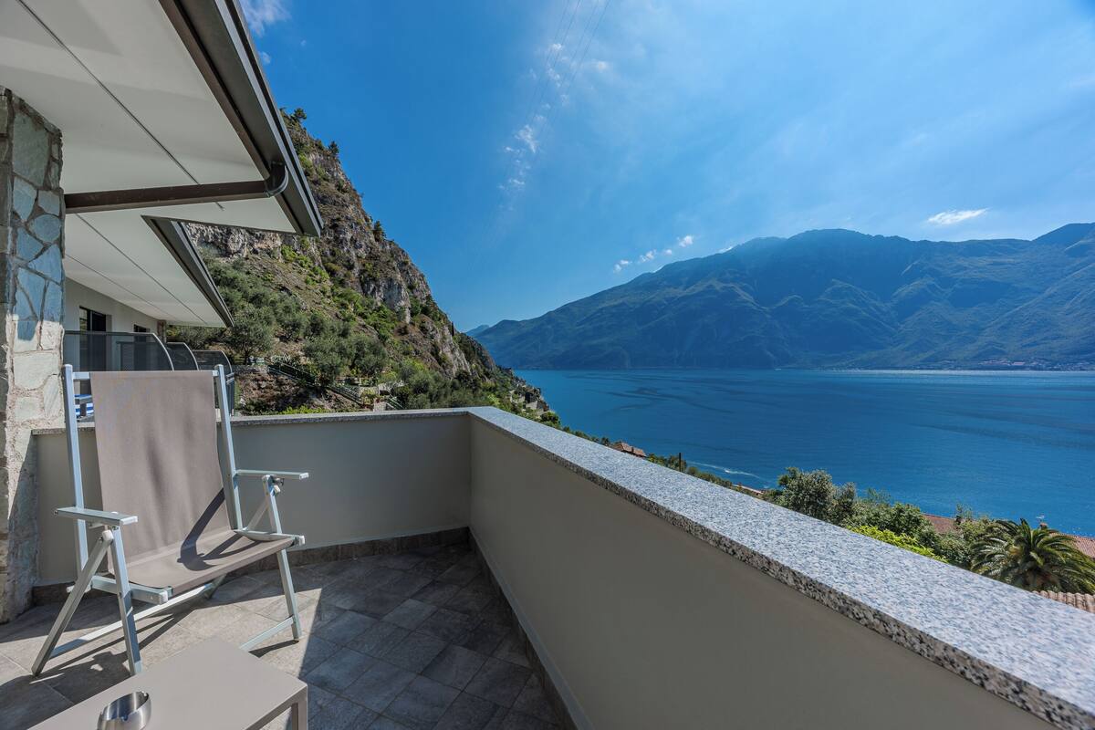 Un balcón con vista a un lago y montañas, una silla y una mesa.