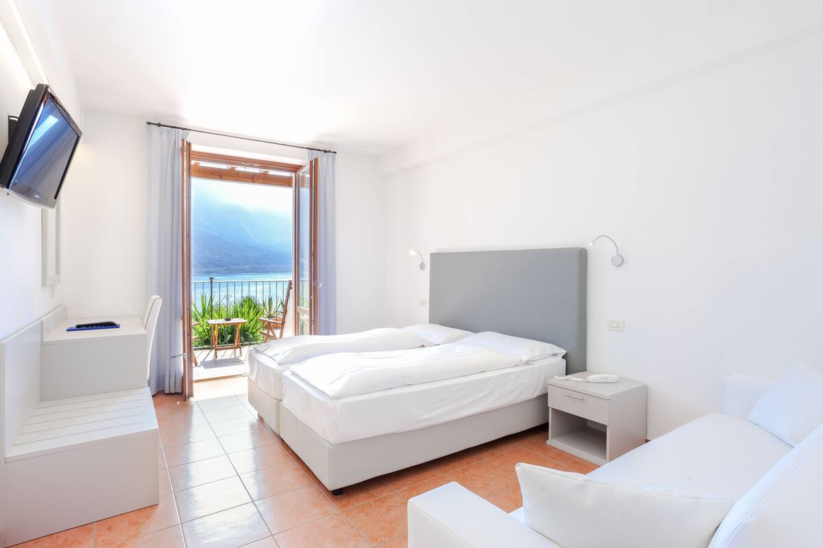 Una habitación de hotel moderna con una cama grande, una mesita de noche, un televisor montado en la pared y un balcón con vistas al mar.