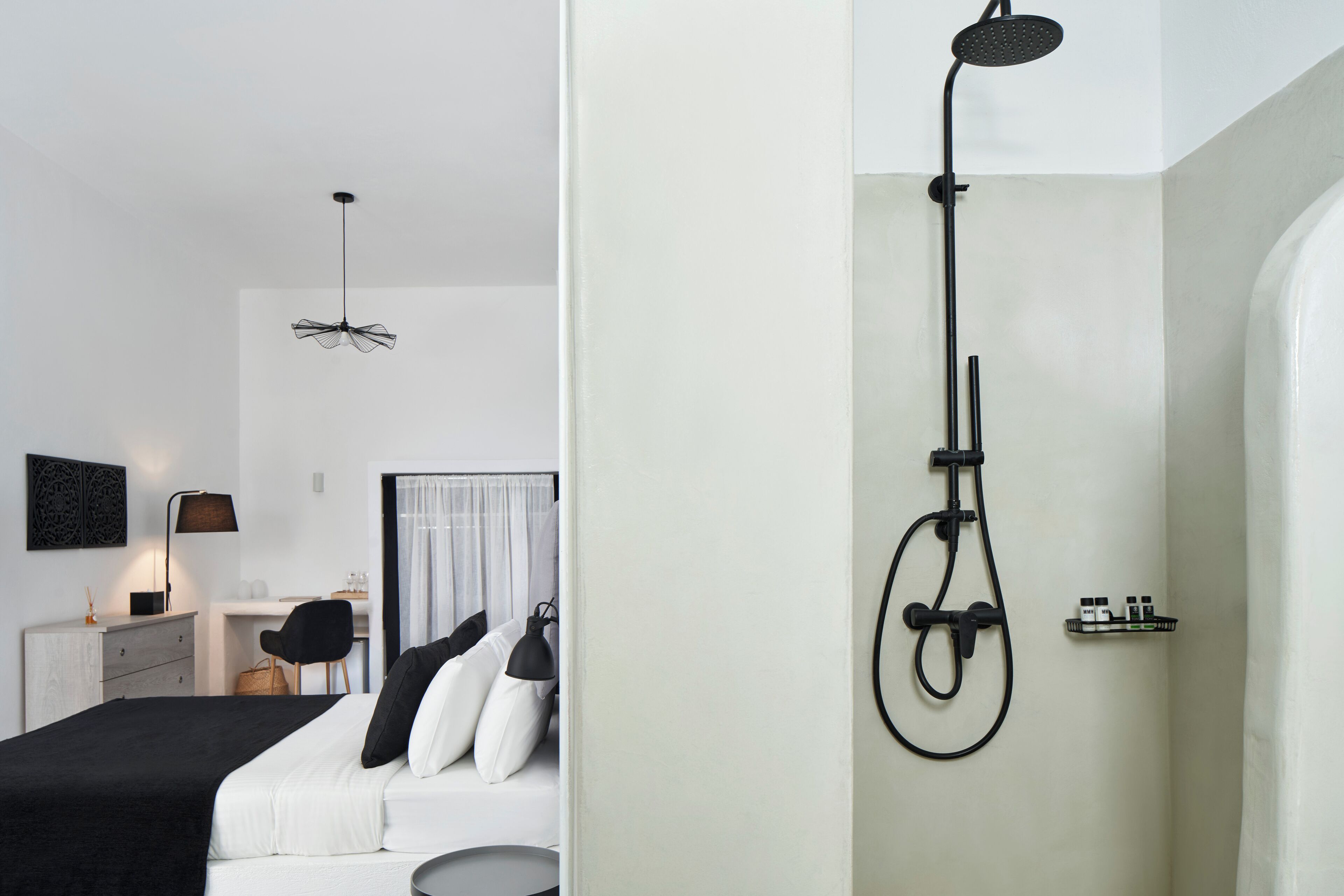 A modern hotel room with a bed, a desk, a chair, a lamp, and a shower.