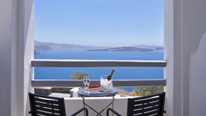 Un balcón con una mesa lista para dos personas, con vistas a un paisaje pintoresco que incluye agua y tierra a lo lejos.
