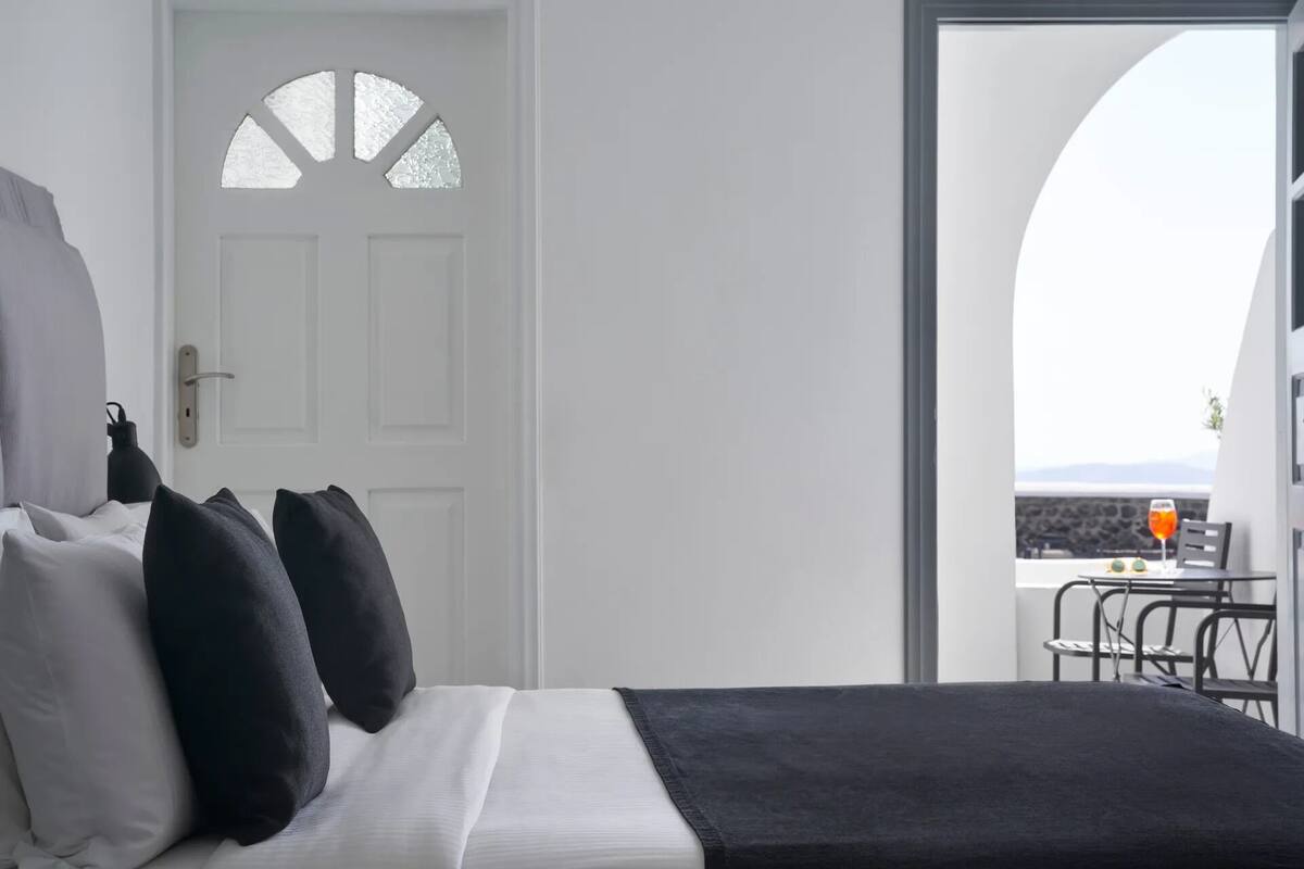 A bedroom with a bed, pillows, a door, and a balcony with a table and chairs.