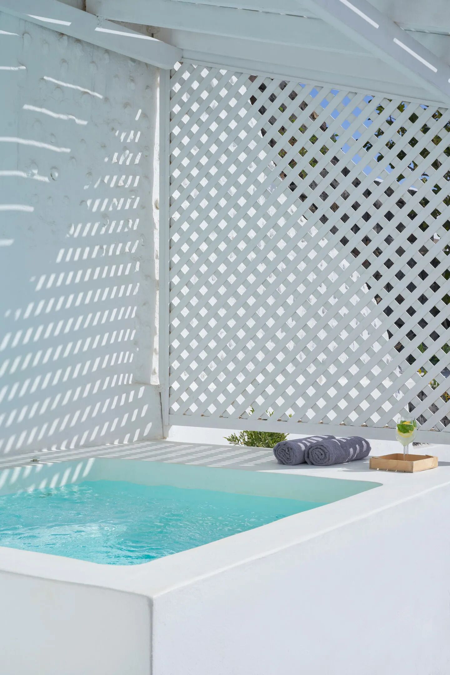 Un área de piscina privada con cercado blanco de celosía, un jacuzzi y una pequeña mesa con una bebida.