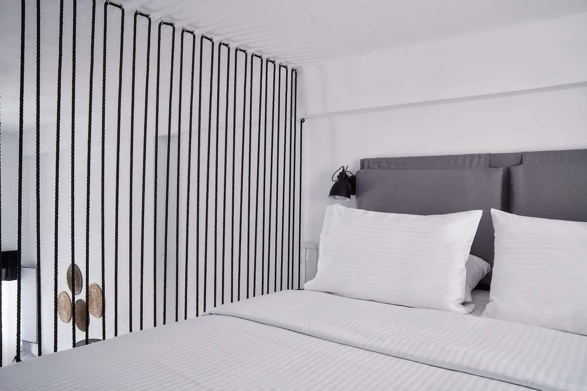 A modern bedroom with a bed, white bedding, a grey headboard, and a black and white striped partition.
