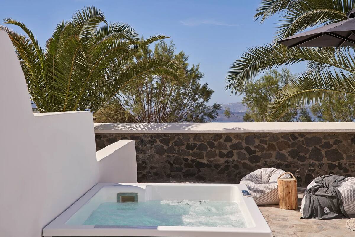 A hot tub with a stone wall backdrop and a view of palm trees.