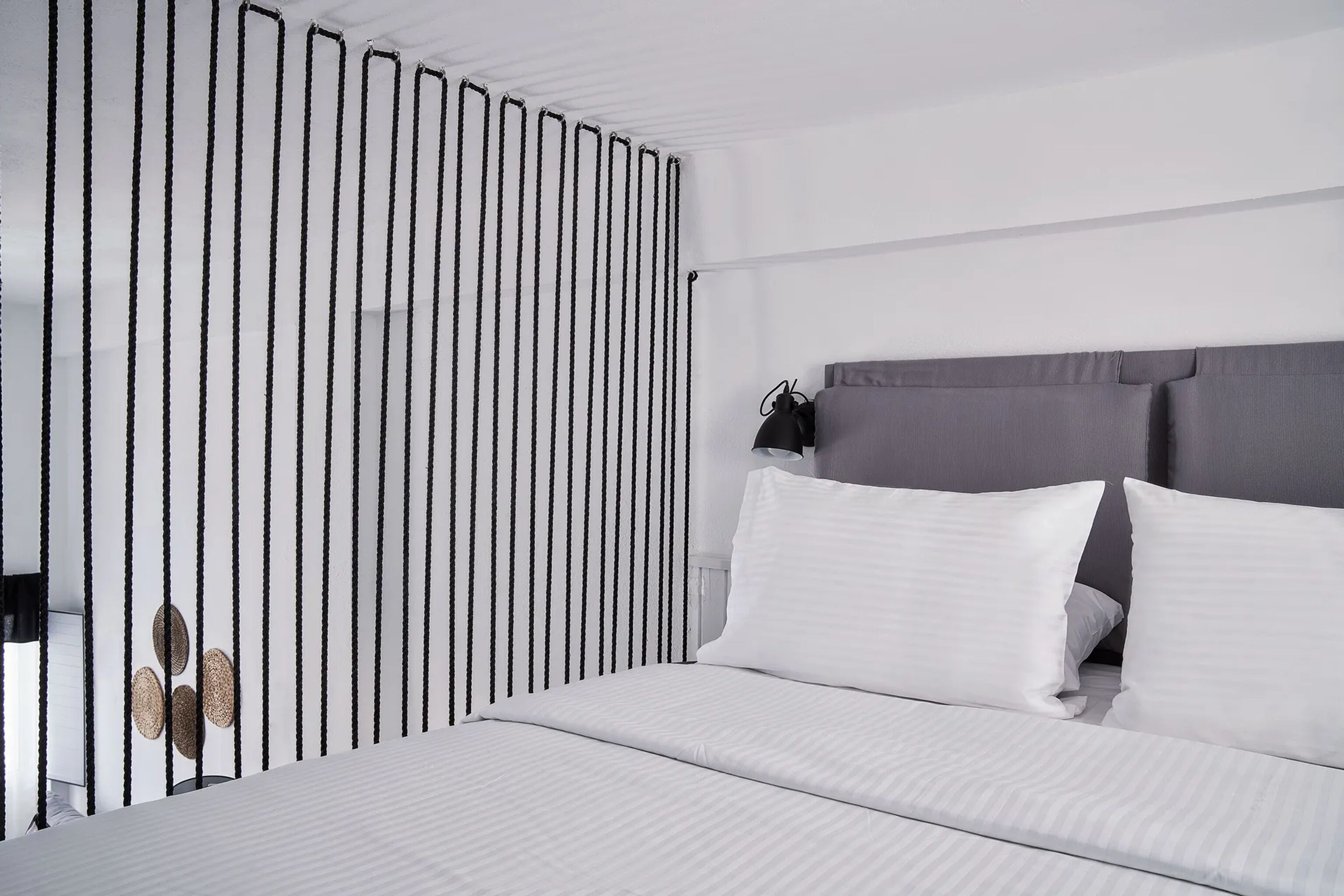 Habitación de hotel moderna con una cama, ropa de cama blanca, cabecero gris y una lámpara negra.