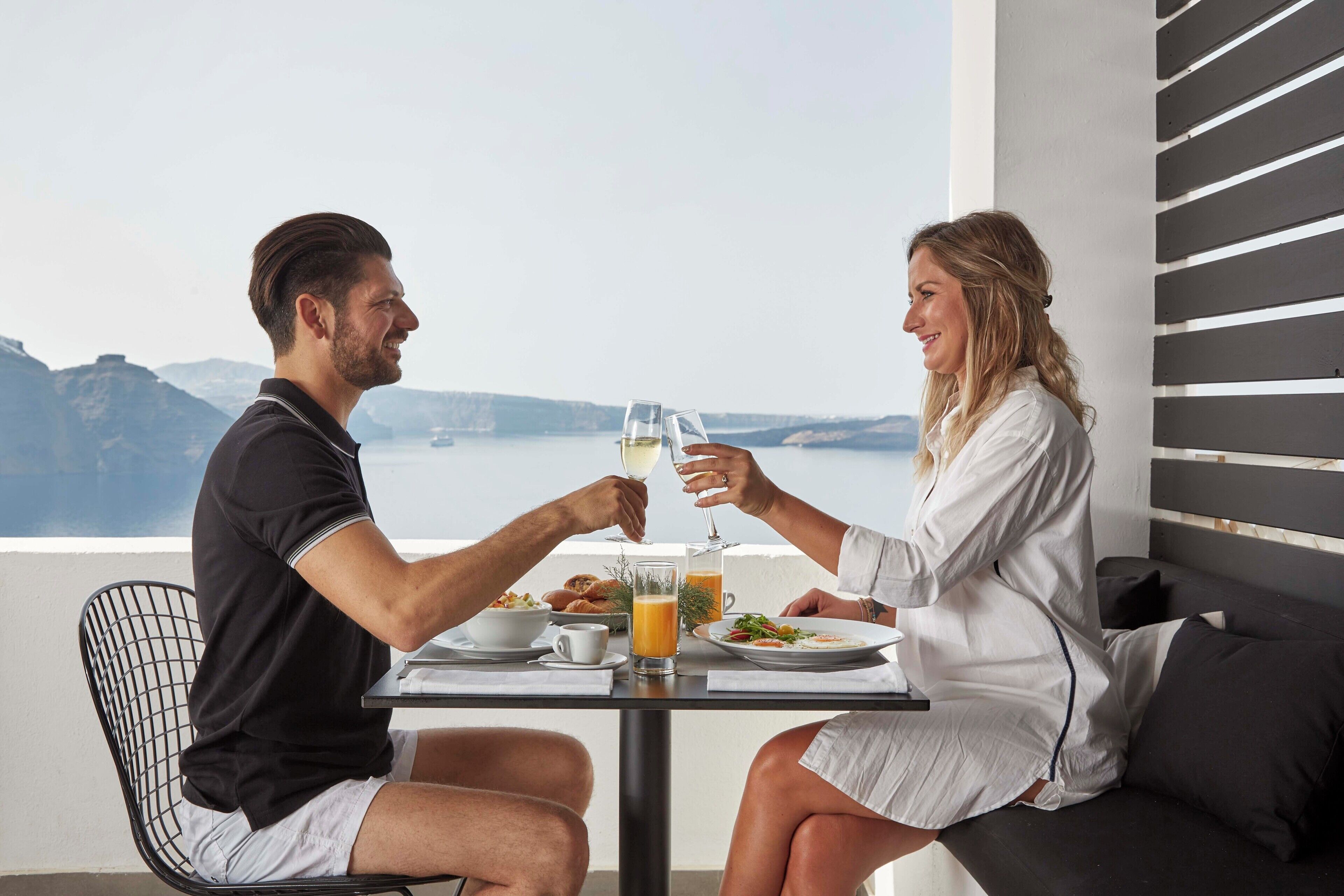 Um casal jantando à mesa com vista para o mar e montanhas.