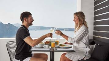 Um casal jantando à mesa com vista para o mar e montanhas.